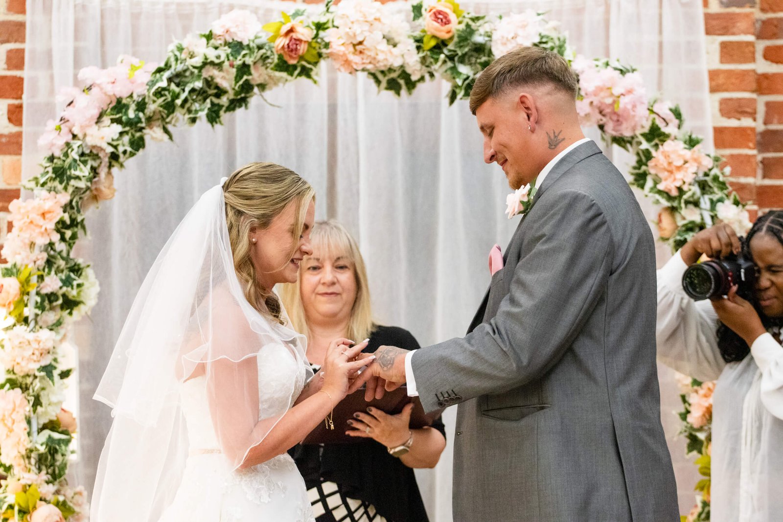 Bride and groom exchanging rings beneath a floral ceremony arch